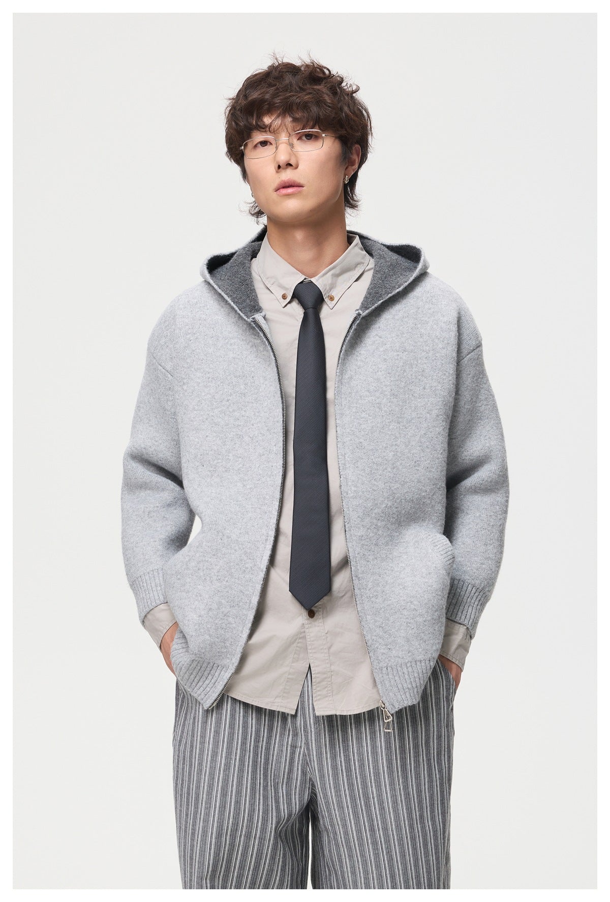Model wearing a light gray zip-front hooded cardigan over a beige shirt and dark tie.