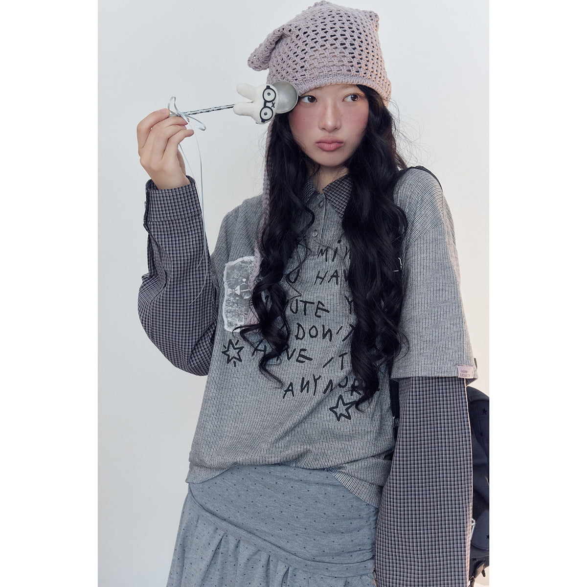 Close view of a model in a gray graphic top with checked layered sleeves and a pale mauve crocheted hat.