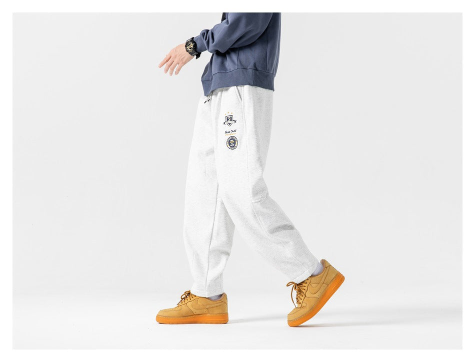 Side view of a model walking in light gray relaxed joggers with embroidered thigh patches.