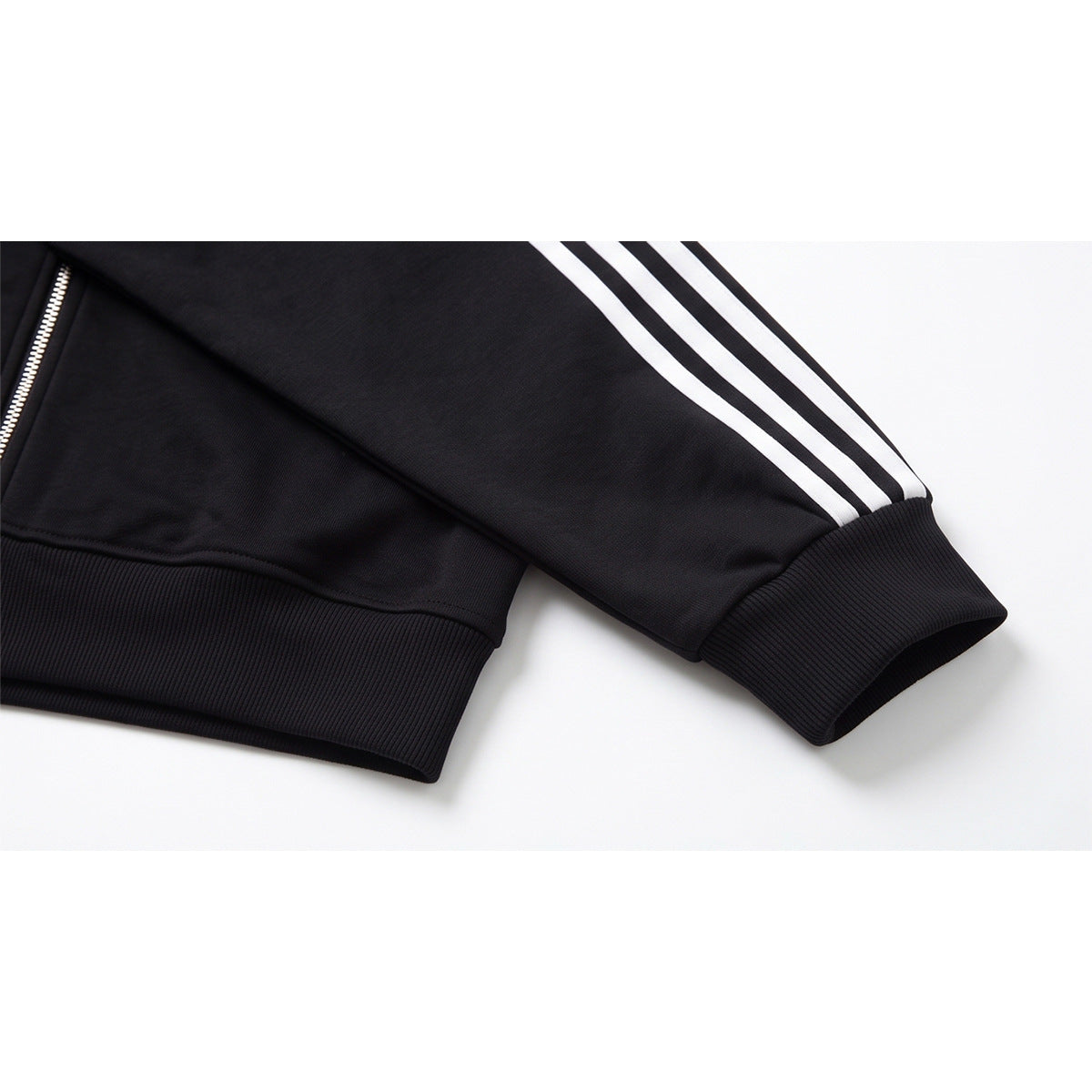 Close-up of a black track jacket sleeve with three white stripes, a ribbed cuff, and ribbed hem.