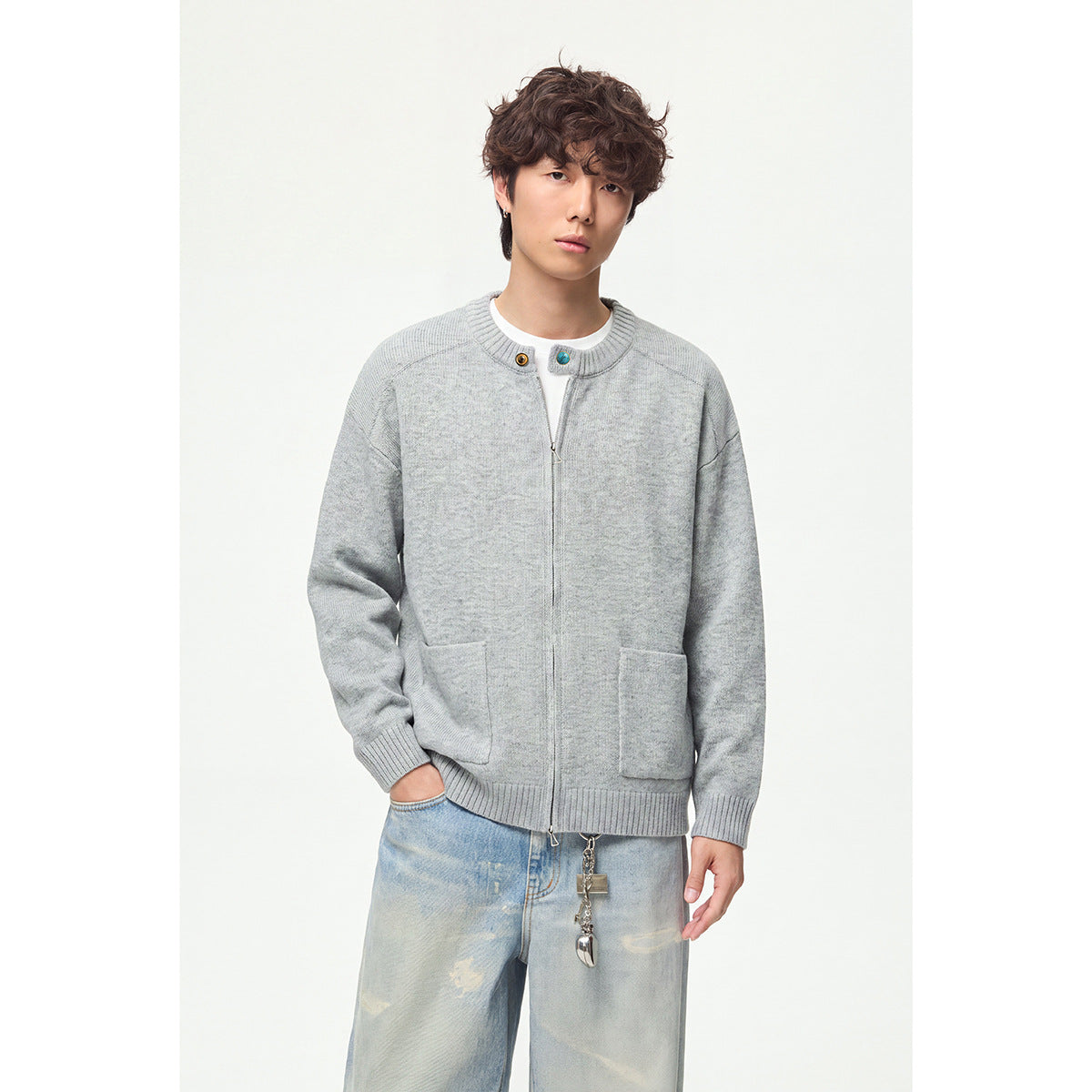 Model wearing a light gray knit cardigan with a front zipper, contrast buttons, ribbed trim and two patch pockets.