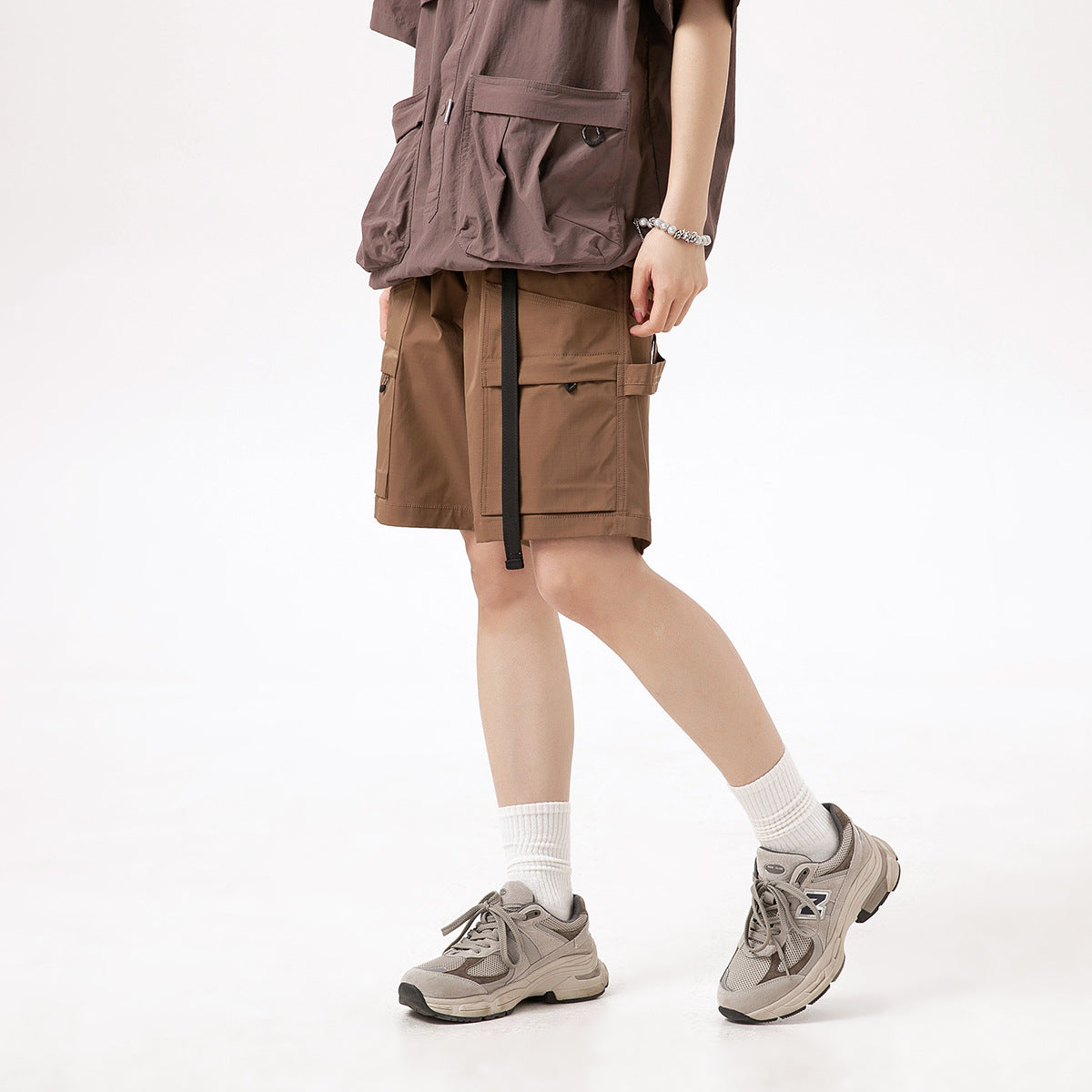 Cropped model wearing brown cargo shorts with large utility pockets and a long black hanging strap.
