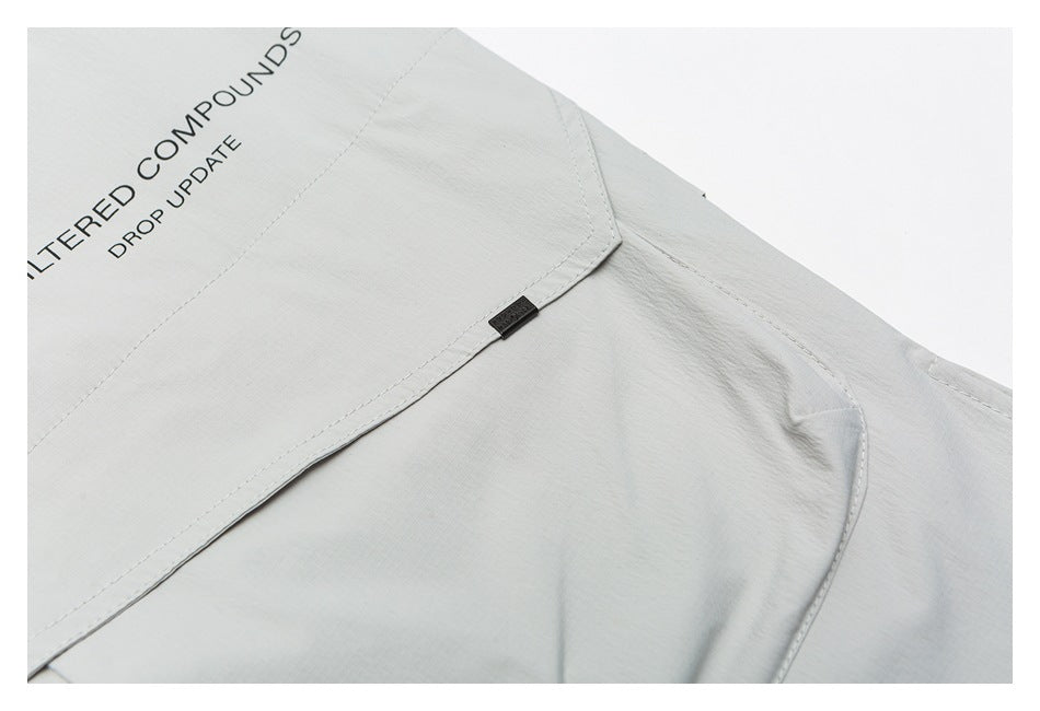 Close-up of the pale gray jacket’s layered back panel, seam, and small dark tab, with part of its printed text visible.
