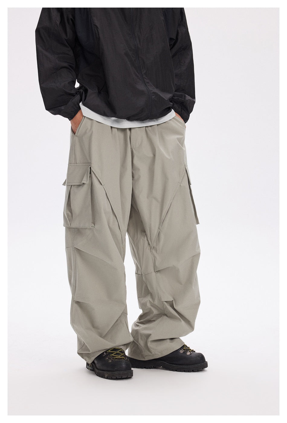 Front view of a model wearing loose light gray cargo pants with large flap pockets and angular panel seams.