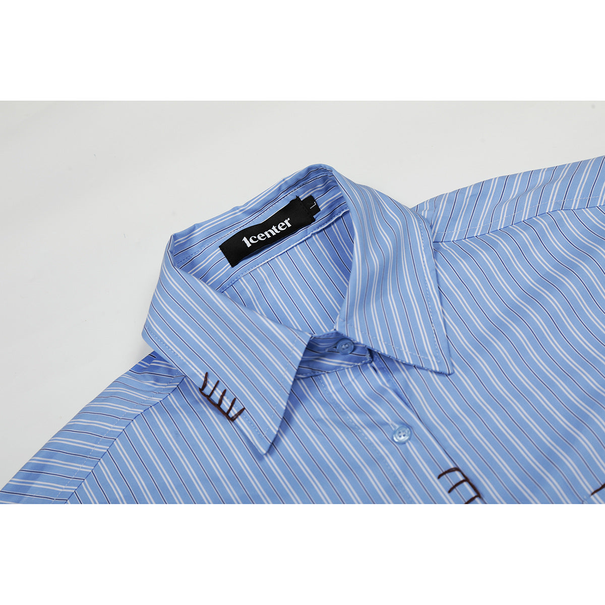 Close-up of a blue-and-white striped shirt collar, buttons, and dark decorative stitching.