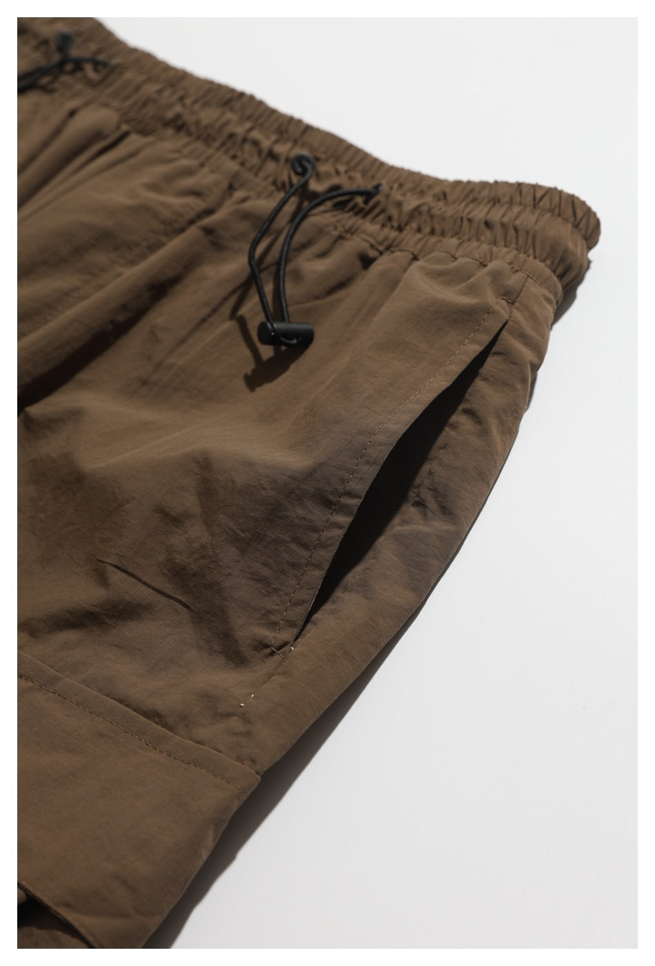 Close-up of the brown shorts' elastic waistband, black drawcord, and side pocket.