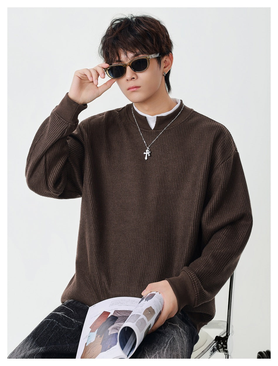 Model wearing brown ribbed pullover with white inner collar, holding sunglasses and a magazine