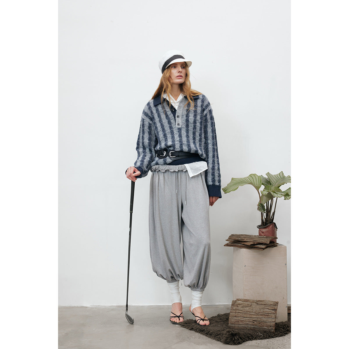 Model wearing a gray-and-navy striped pullover with a polo collar, gray joggers, and a white hat.