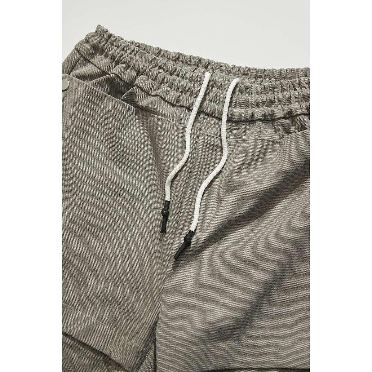 Close-up of gray-beige trousers with a gathered elastic waist, white drawstrings, and a front pocket.