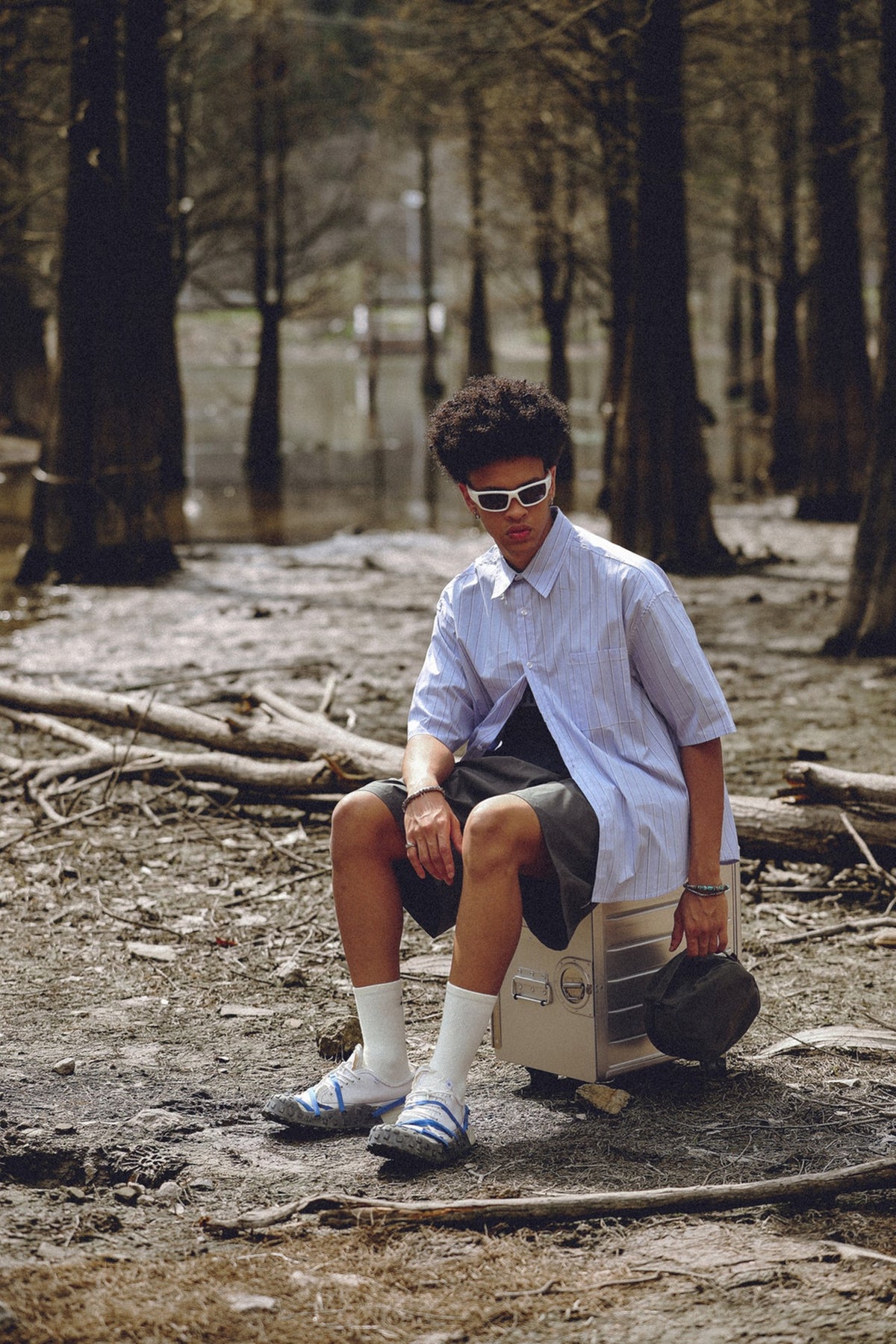 Seated model wearing an oversized pale blue pinstriped short-sleeve button-up shirt with a chest pocket.