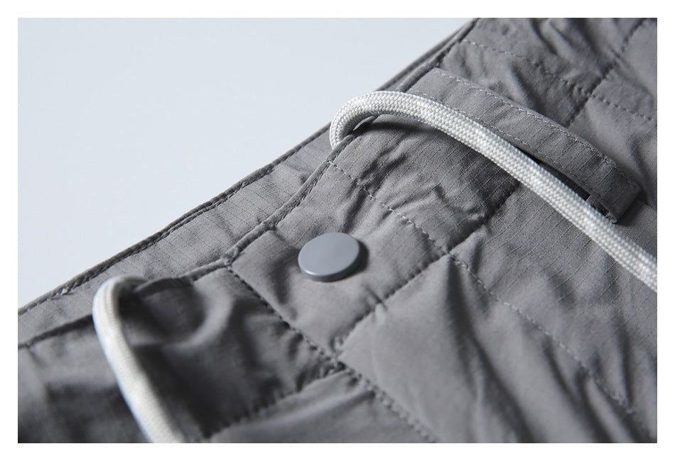 Close-up of gray pants showing a snap at the waistband and a white braided drawcord.