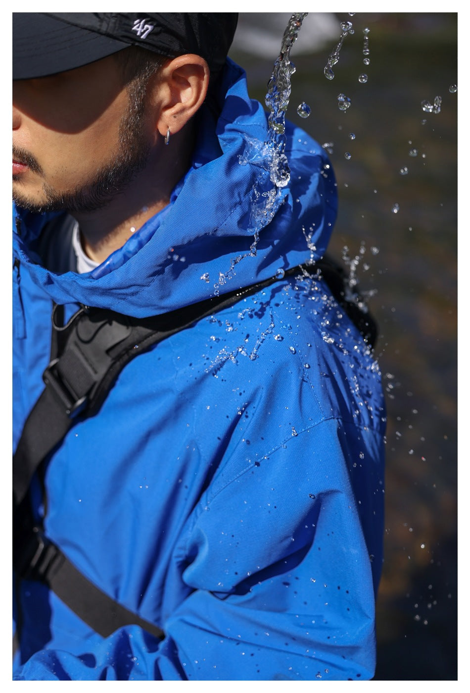 Close-up of a man wearing a blue hooded jacket as water splashes across the shoulder and hood.