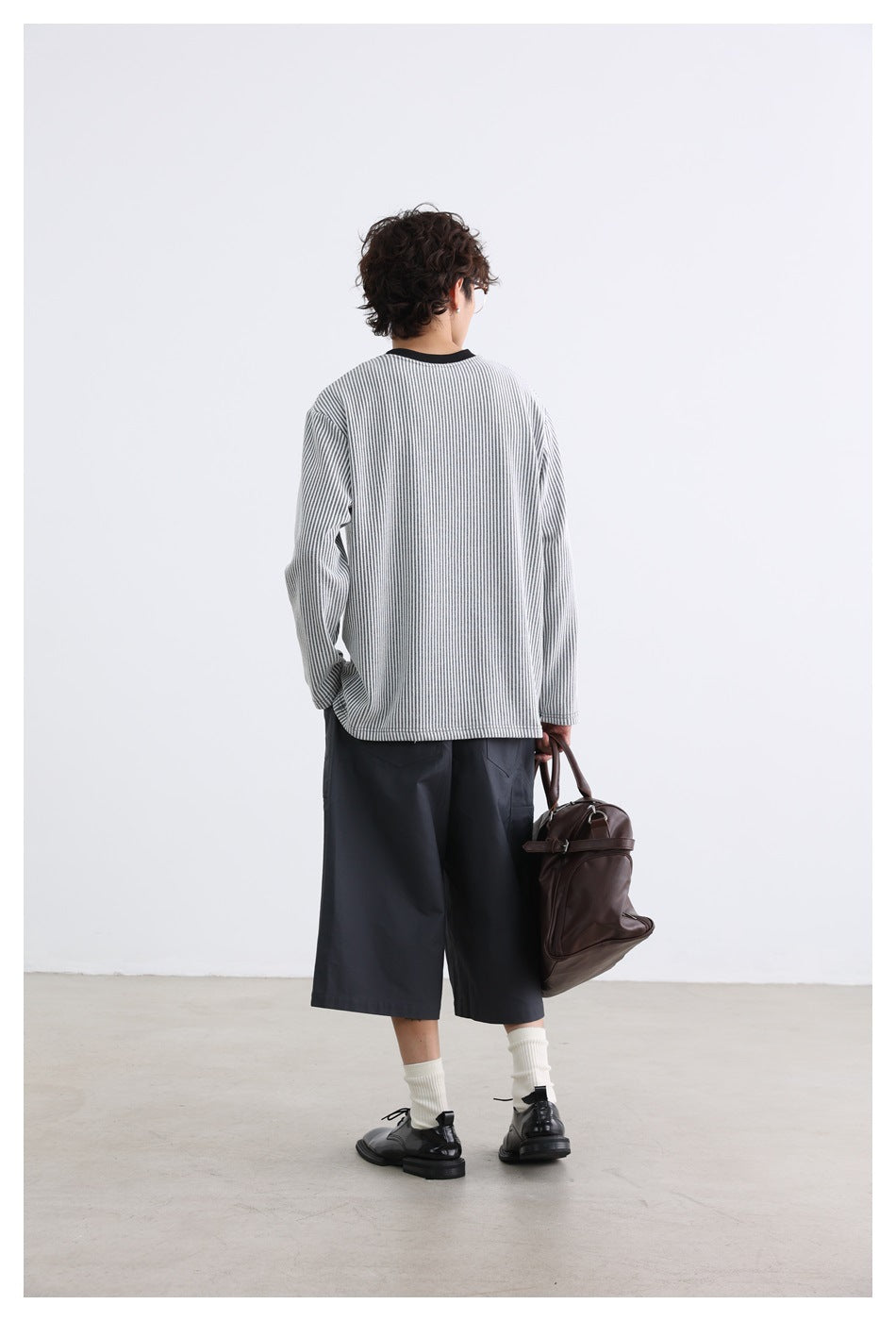 Back view of a model wearing a gray-and-white striped long-sleeve crewneck and dark shorts.