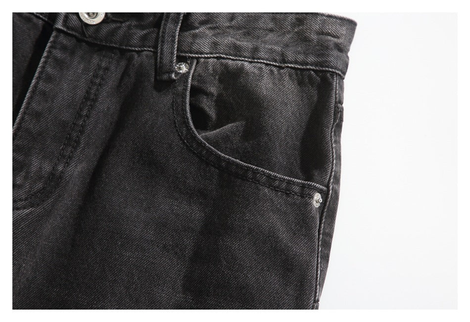 Close-up of a front pocket on black washed jeans, showing its curved opening, rivets and belt loop.