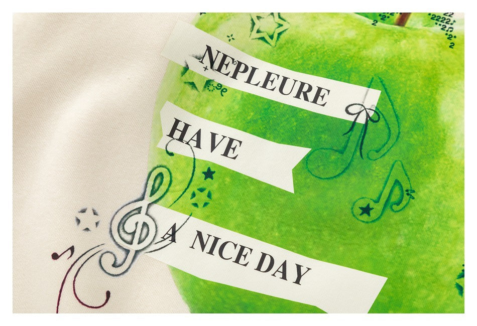 Close-up of a green apple and musical-note print with “Have a nice day” lettering on cream fabric.