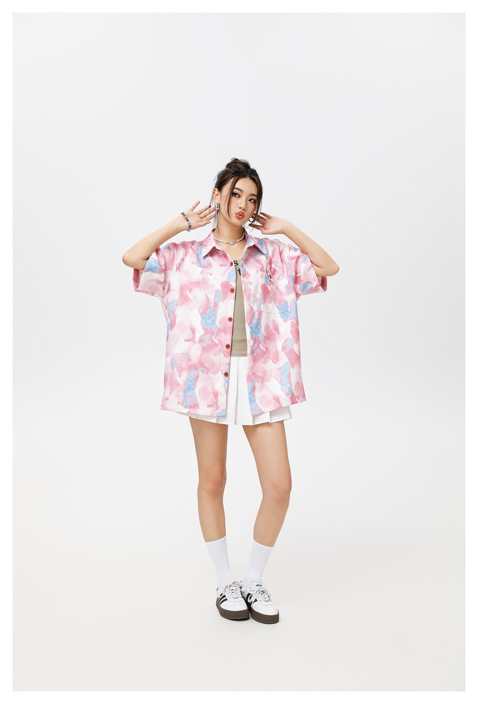 Model in a pink and light blue print short-sleeve button shirt worn open with a white pleated skirt and sneakers