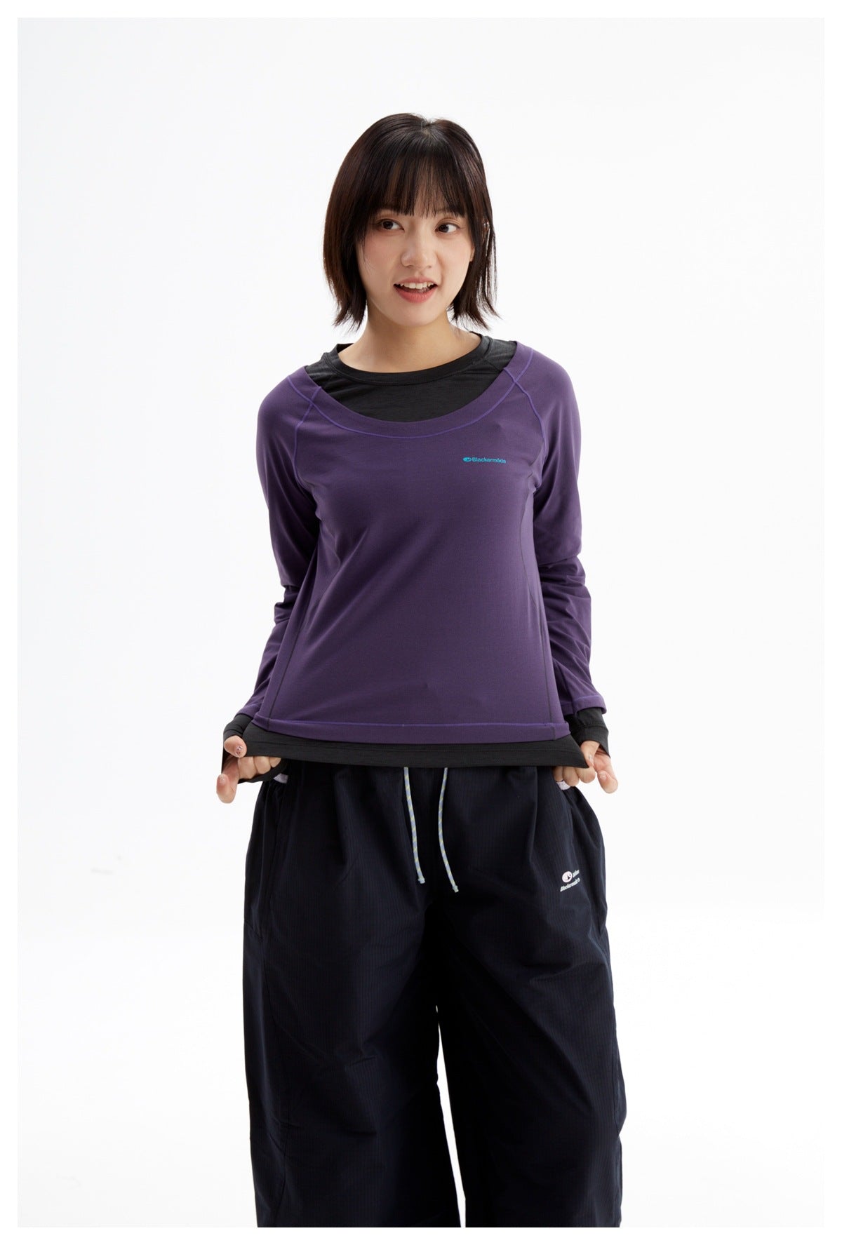 Front view of a model wearing a purple long-sleeve top over a black layer and loose black pants.