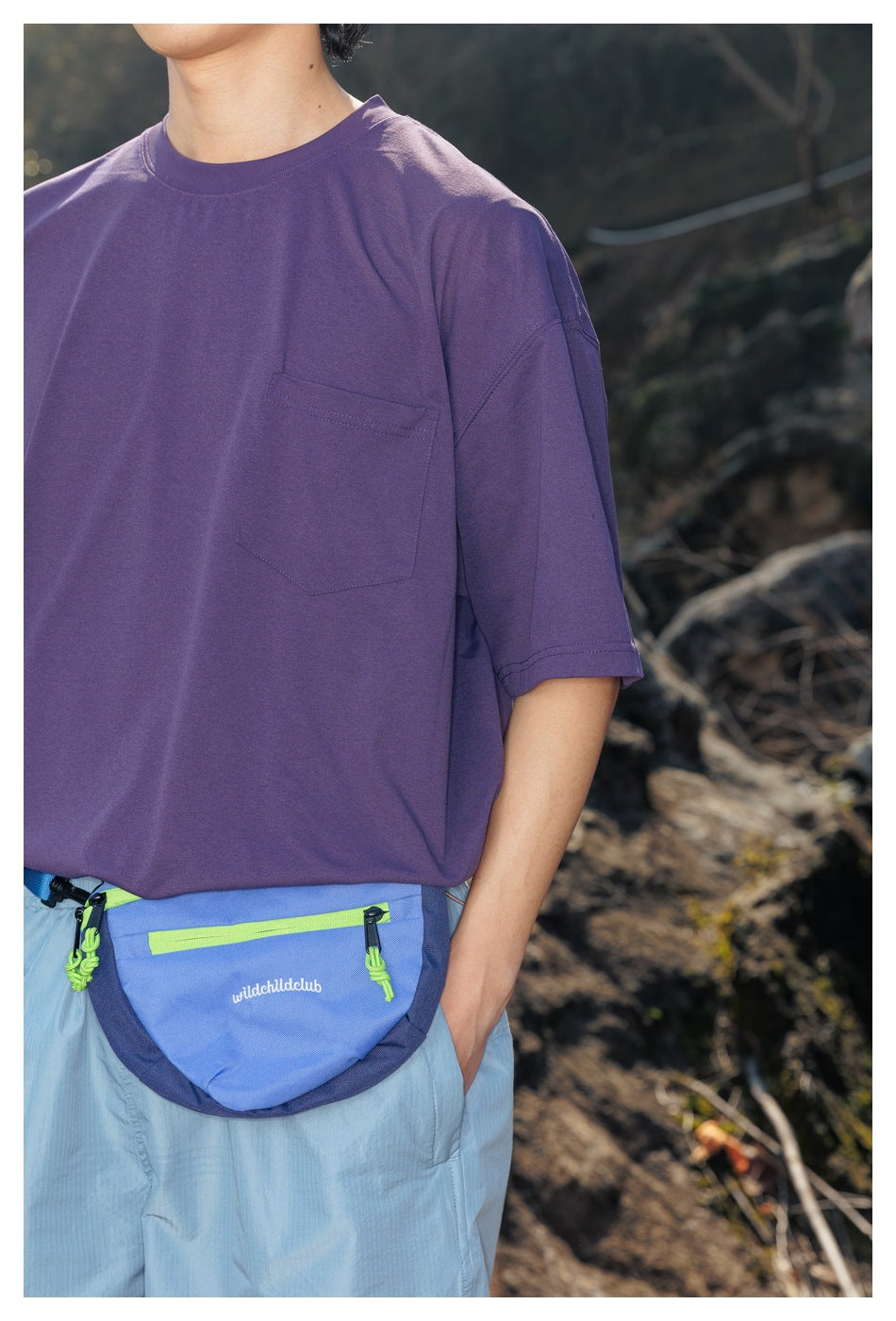 Close-up of a purple oversized T-shirt with a chest pocket, worn above a blue waist pack.