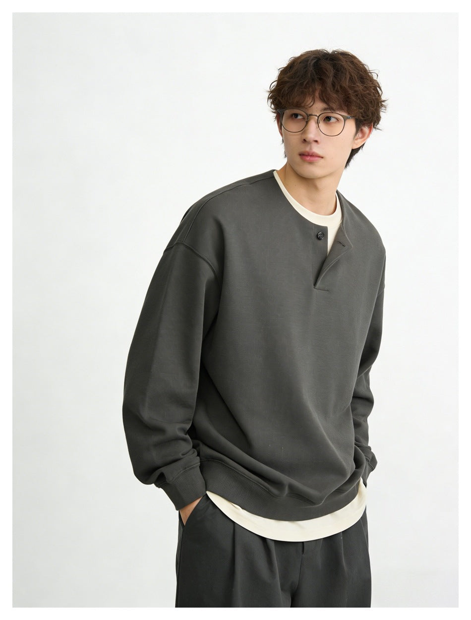 Model wearing a charcoal oversized button-placket sweatshirt over a cream shirt.