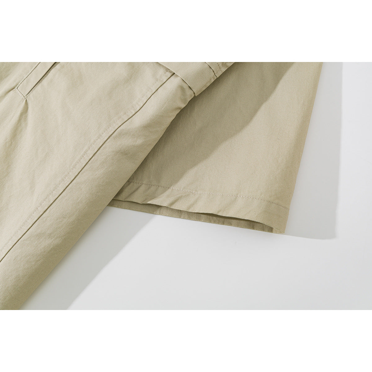 Close-up of the light beige shirt's short sleeve and stitched hem laid flat.