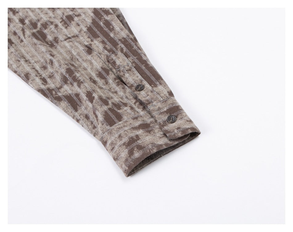 Close-up of a long sleeve and buttoned cuff on a brown and beige patterned shirt.