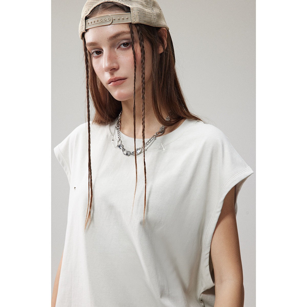 Front view of a model wearing a white sleeveless top with wide armholes and a small chest emblem.
