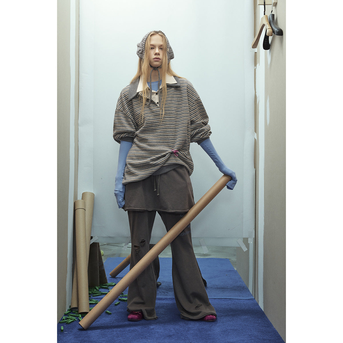 Standing model in a loose gray striped polo with blue sleeves and wide dark trousers.