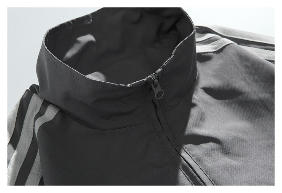 Close-up of a charcoal track jacket's stand collar, front zipper pull, and white shoulder stripes.