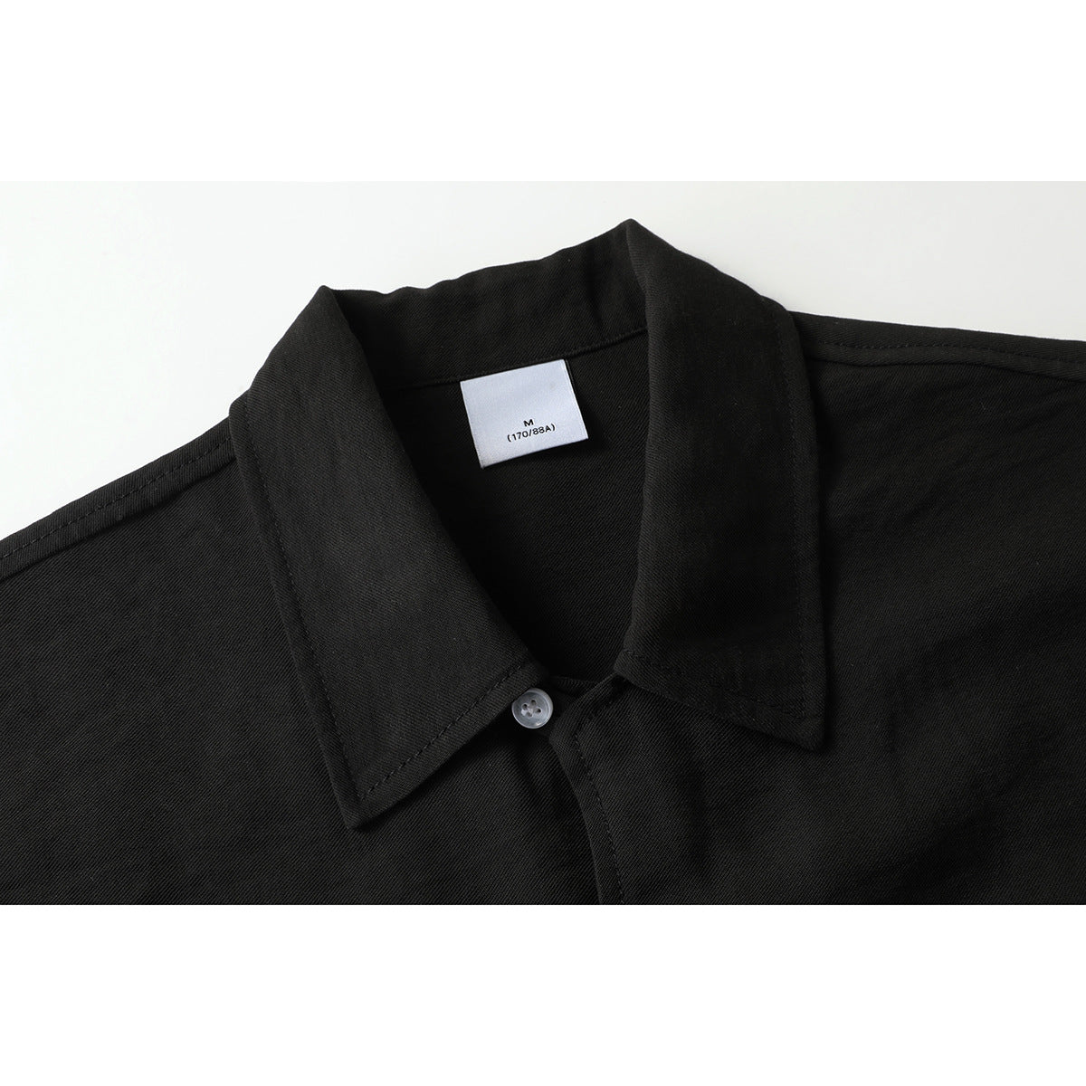 Close-up of a black short-sleeve shirt's pointed collar, white button, and inner size label.
