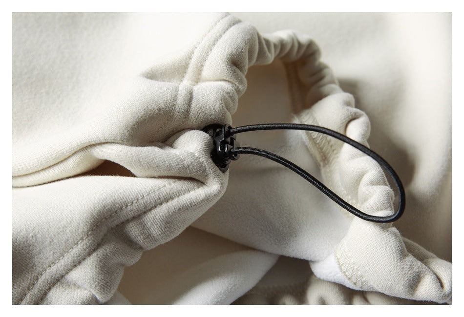 Close-up of a black drawcord toggle at the gathered hem of a cream sweatshirt.