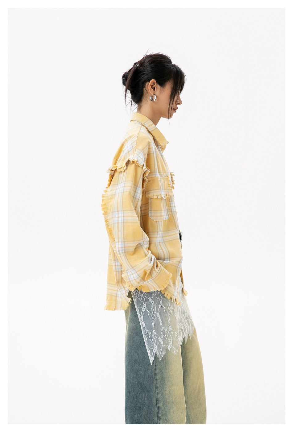Side view of a model in a yellow plaid shirt with frayed trim, white lace hem layer and faded blue jeans