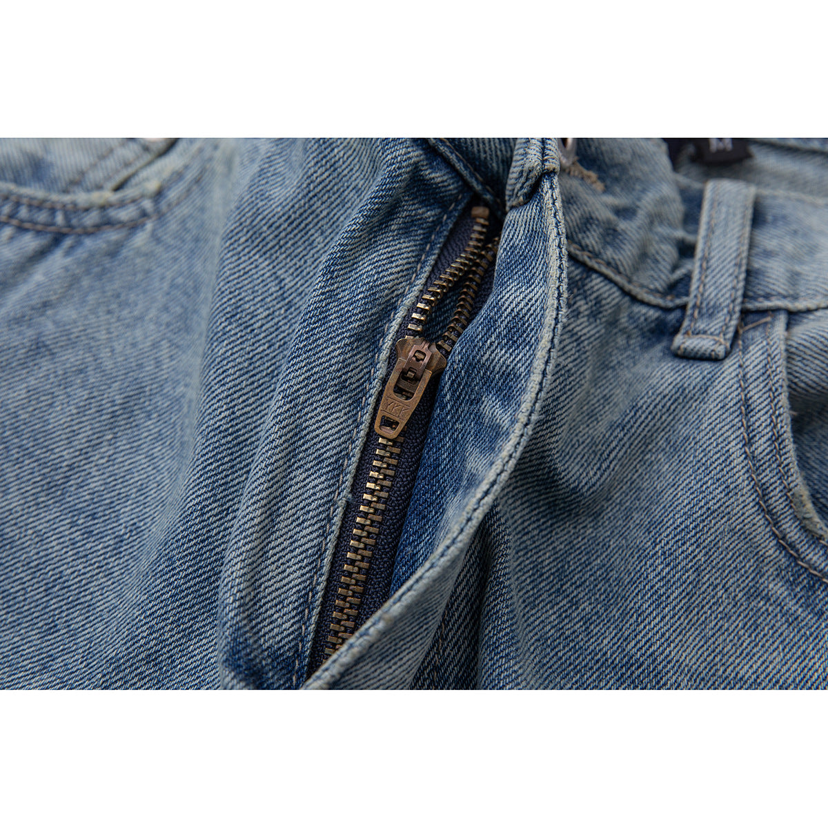 Close-up of the metal zipper and fly on light blue washed jeans.
