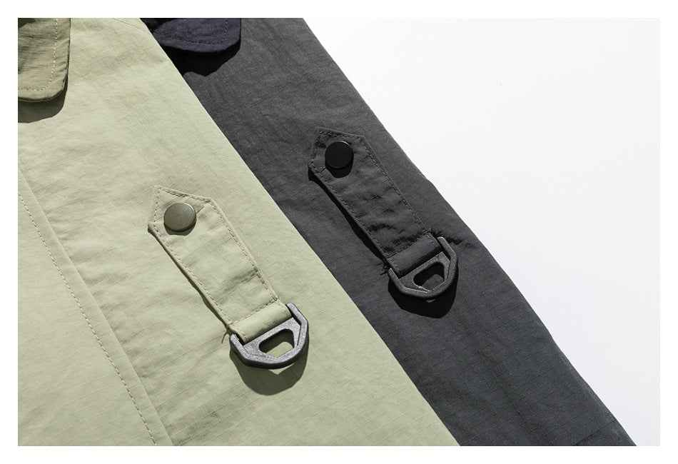 Close-up of olive and charcoal garment panels with snap-fastened utility tabs and metal loops.