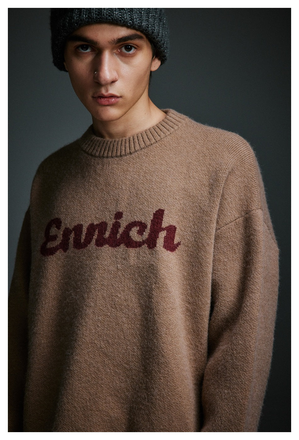 Close view of a model wearing a taupe crewneck sweater with burgundy script lettering and a dark knit beanie.