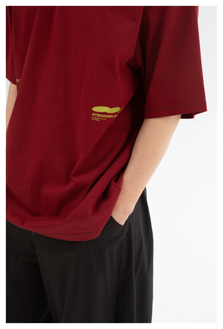 Close-up of a burgundy T-shirt’s small yellow-green side print, sleeve, and hem on a model.