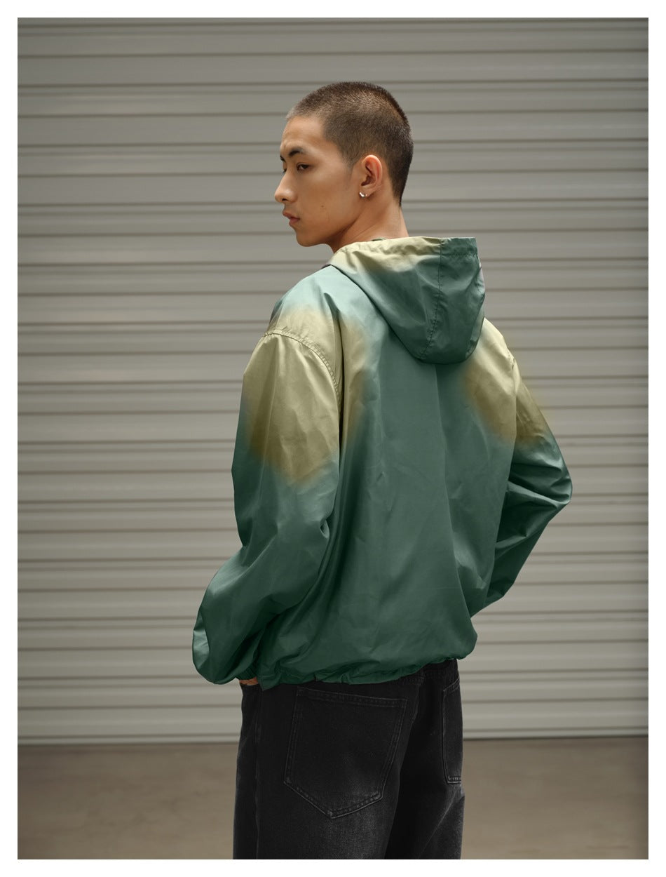 Back view of a model wearing a sage green hooded jacket with olive accents across the shoulders and sleeves.