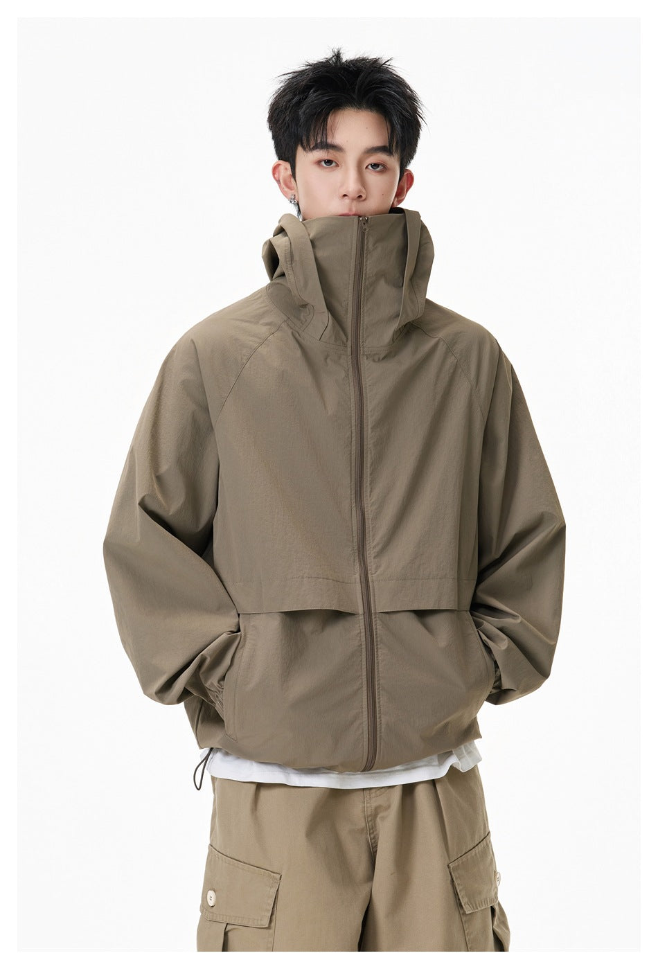 Front view of a model wearing an olive-brown hooded zip jacket with a high collar and tan cargo shorts.