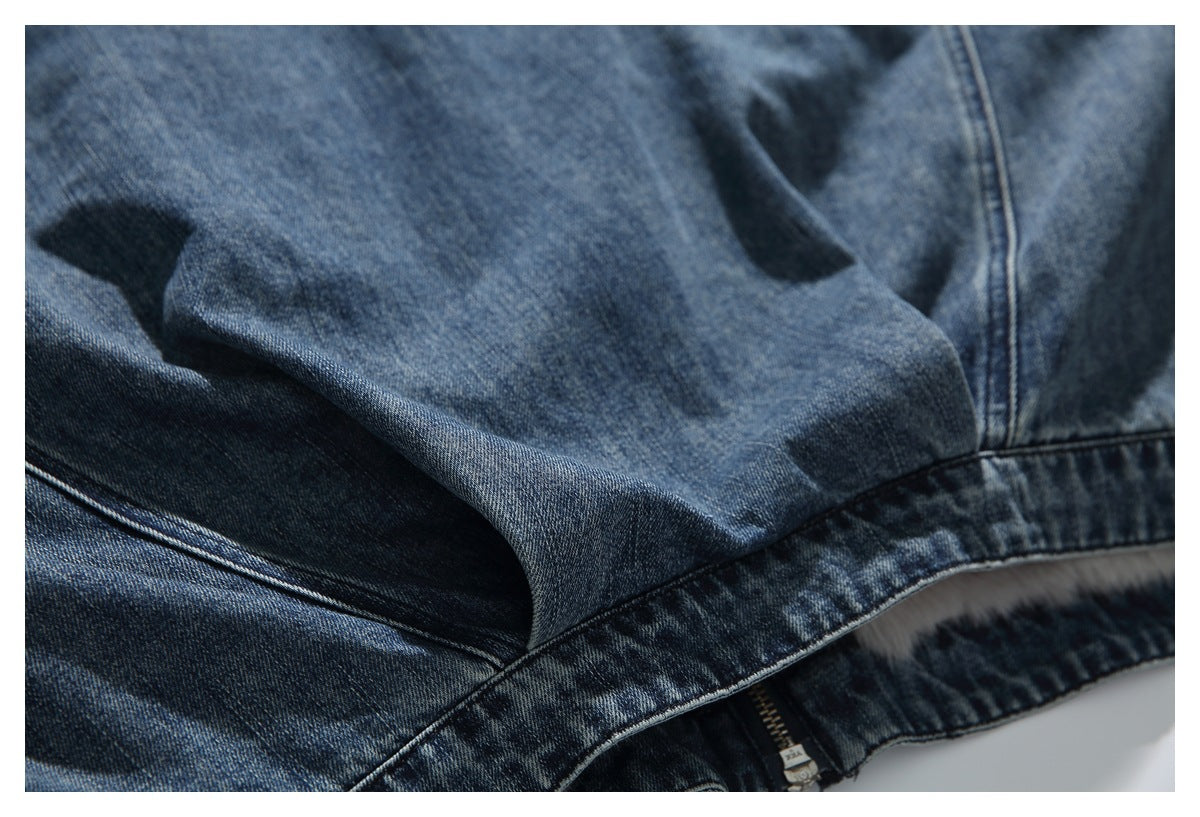 Close-up of a pocket seam and zipper at the lower edge of a washed blue denim jacket.