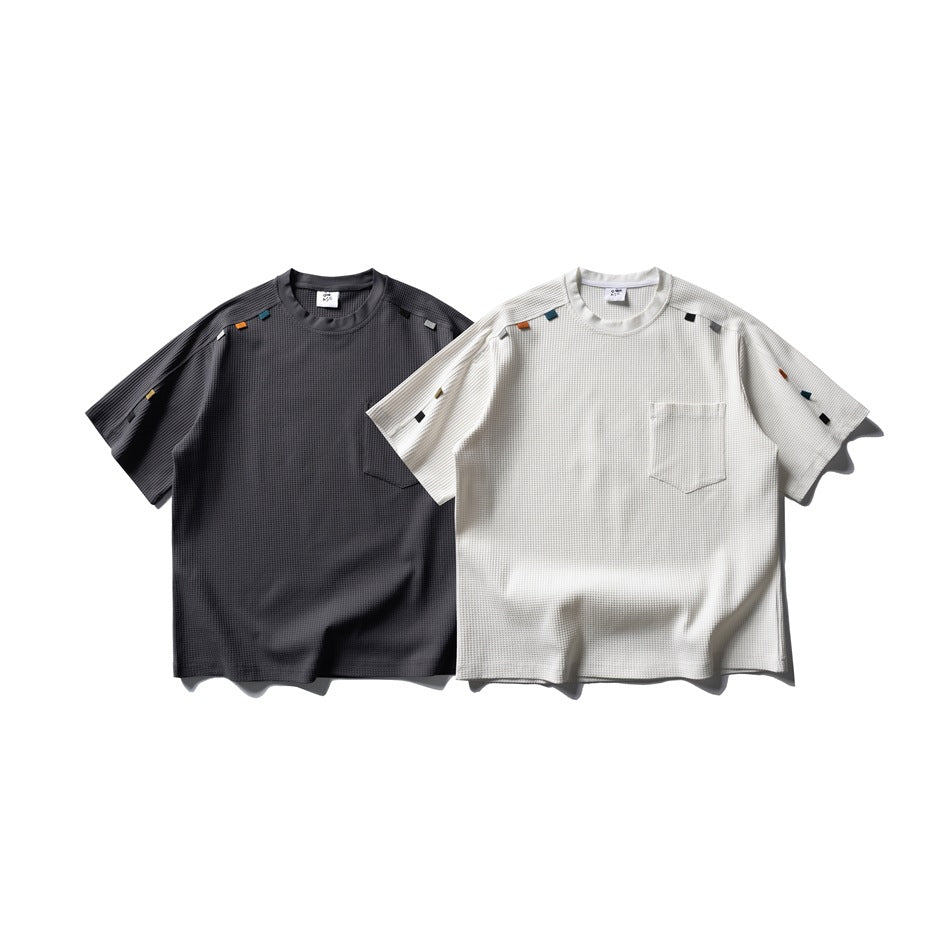 Front view of charcoal and ivory short-sleeve waffle-textured shirts with chest pockets and colorful fabric tabs.