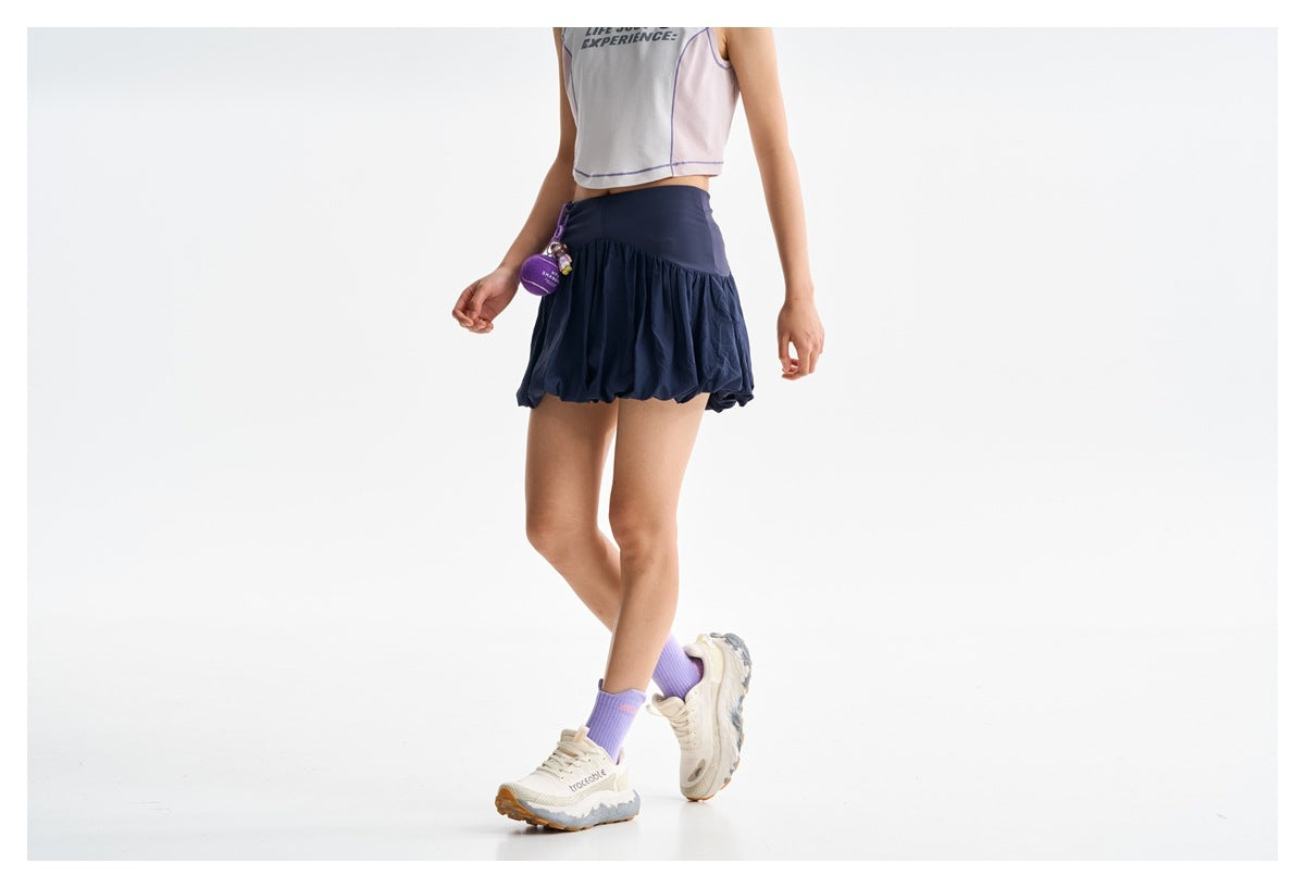 Cropped model wearing a navy bubble-hem tennis skirt with a wide waistband and a white cropped top.