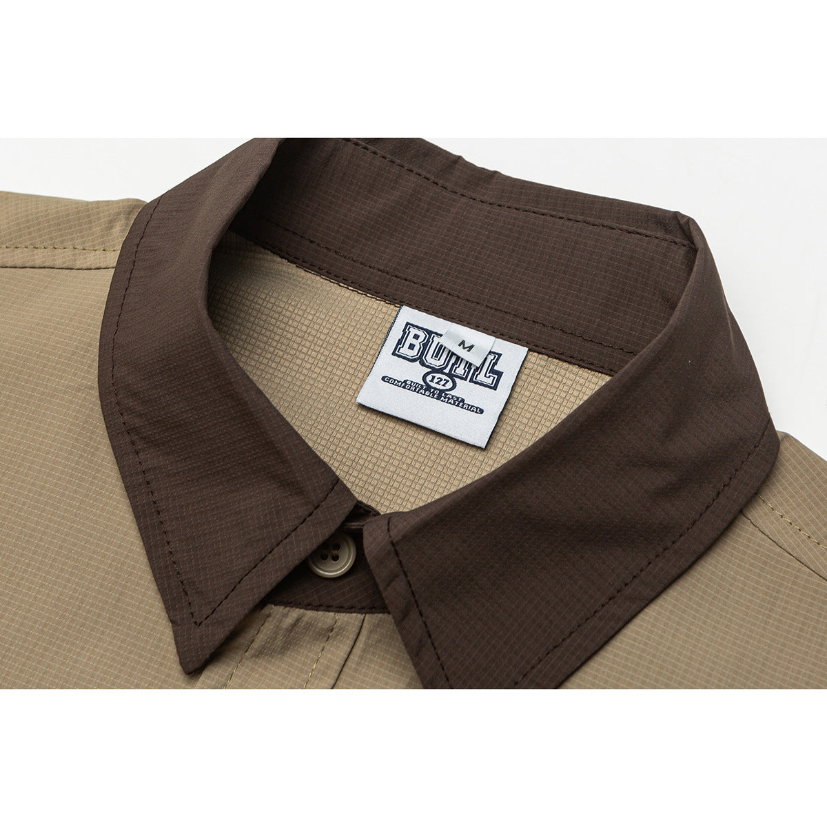Close-up of a tan shirt with a dark brown pointed collar, button, and visible sewn-in neck label.
