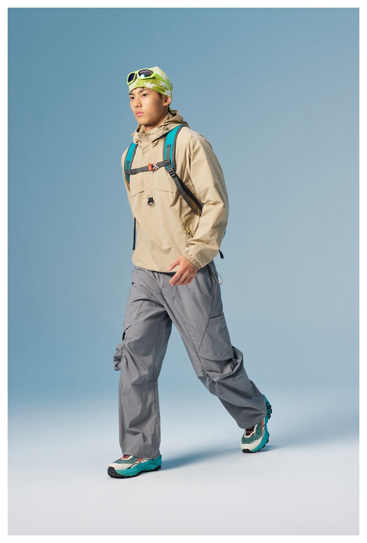 Model wearing a beige hooded pullover, loose gray cargo pants and a teal-strapped backpack.