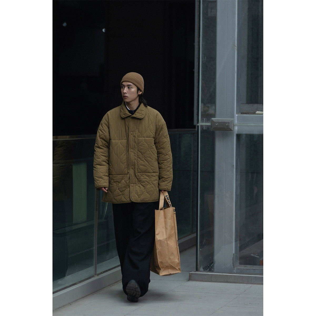 Full-length view of a model wearing an olive-brown quilted coat with a collar and front buttons.