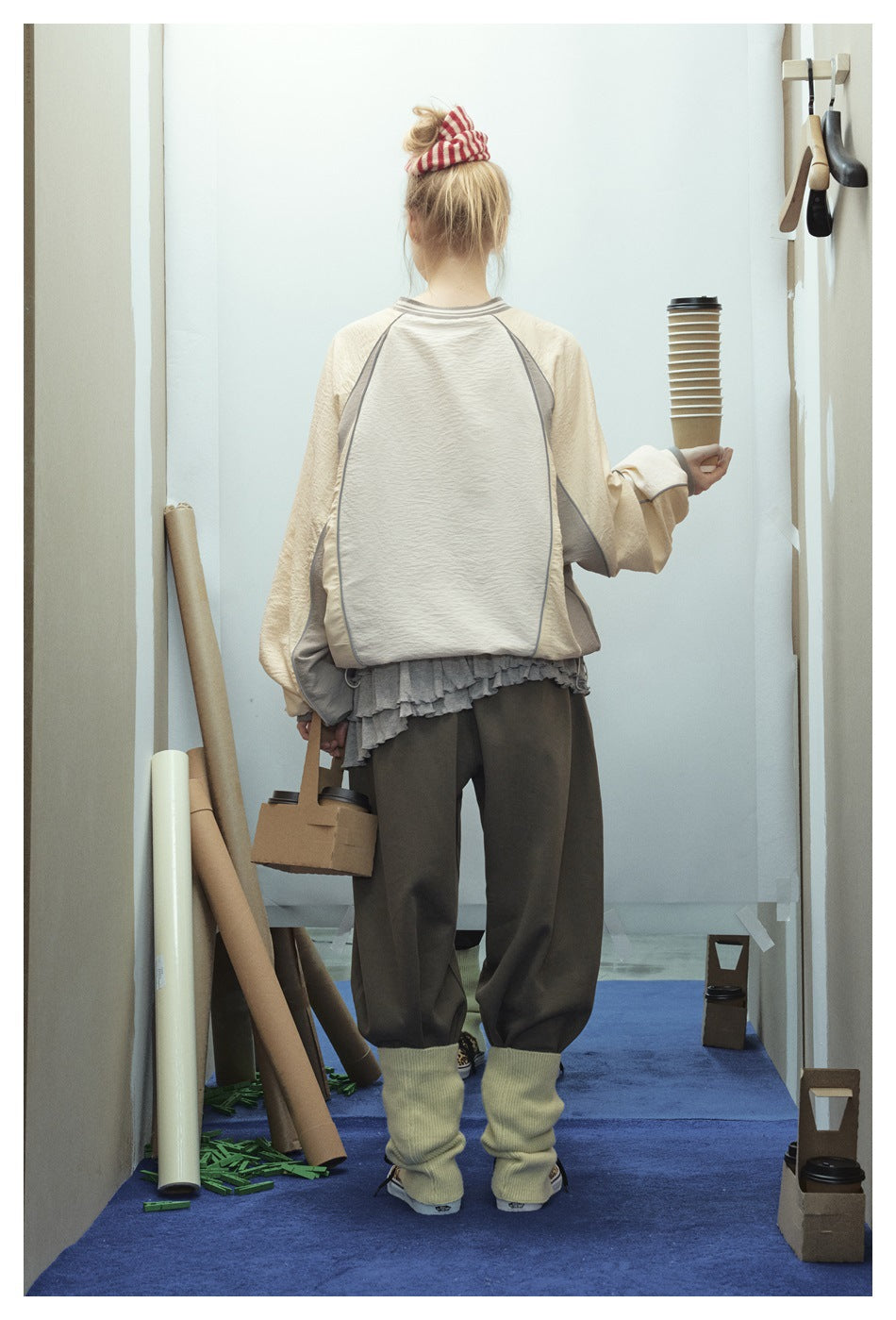 Rear view of a model wearing a cream-and-gray color-block pullover with loose dark trousers and pale leg warmers.