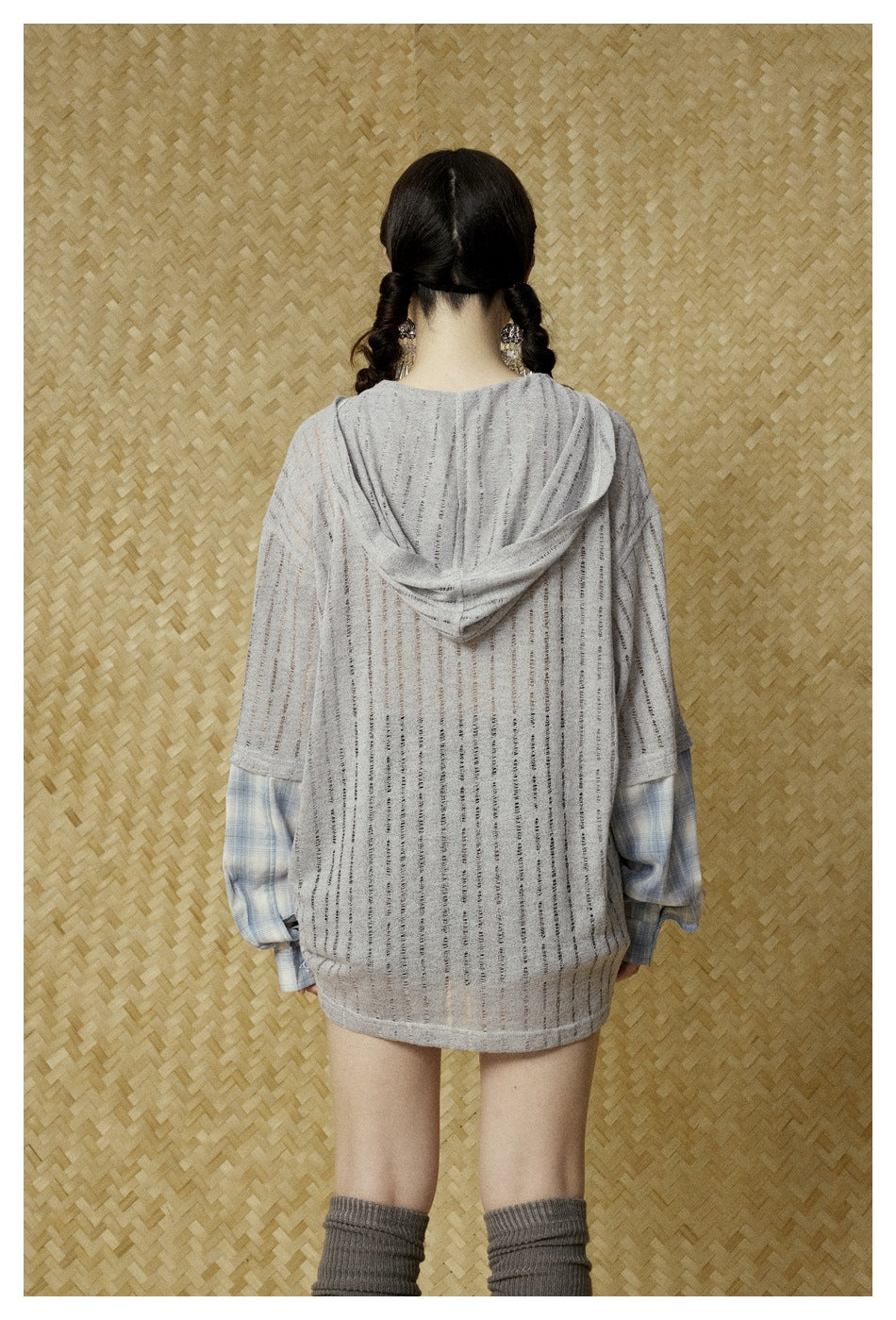 Back view of a model wearing a long light gray striped hooded top with blue plaid sleeves.