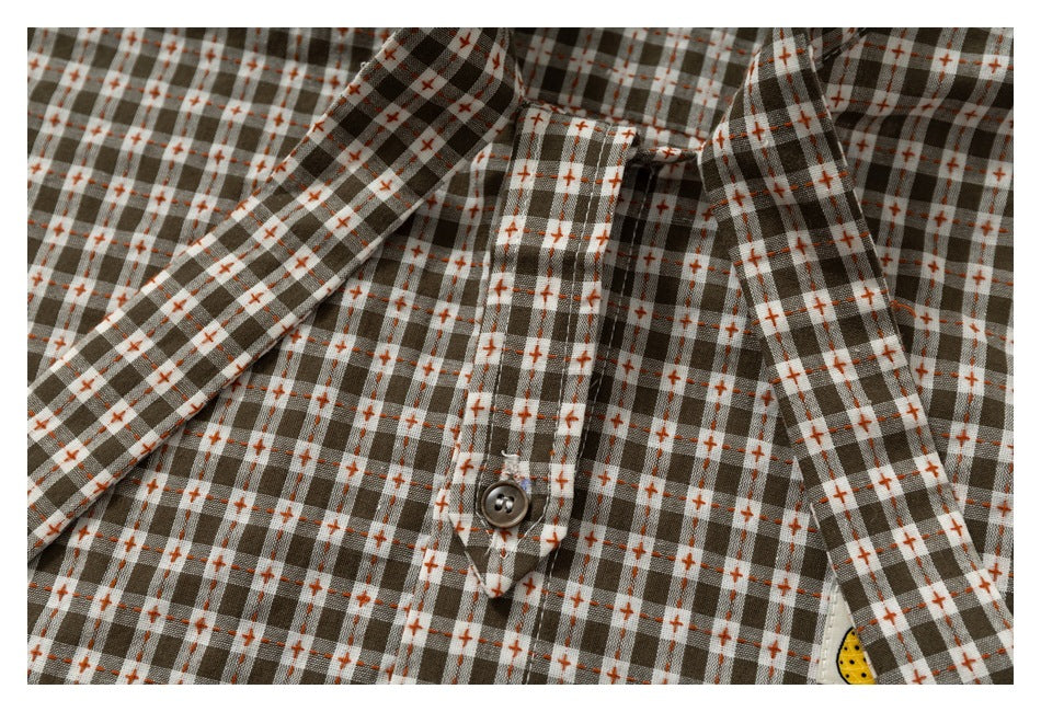 Close-up of a brown, gray, and cream checked shirt front with orange cross-stitch accents and a button.