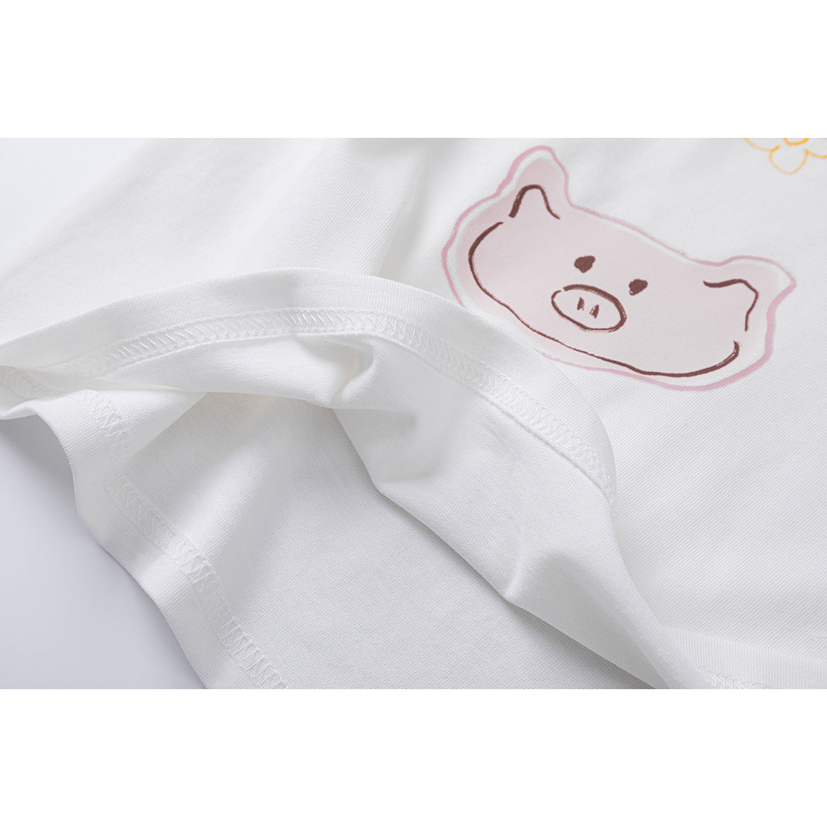 Close-up of a white T-shirt's stitched hem and pink pig illustration.