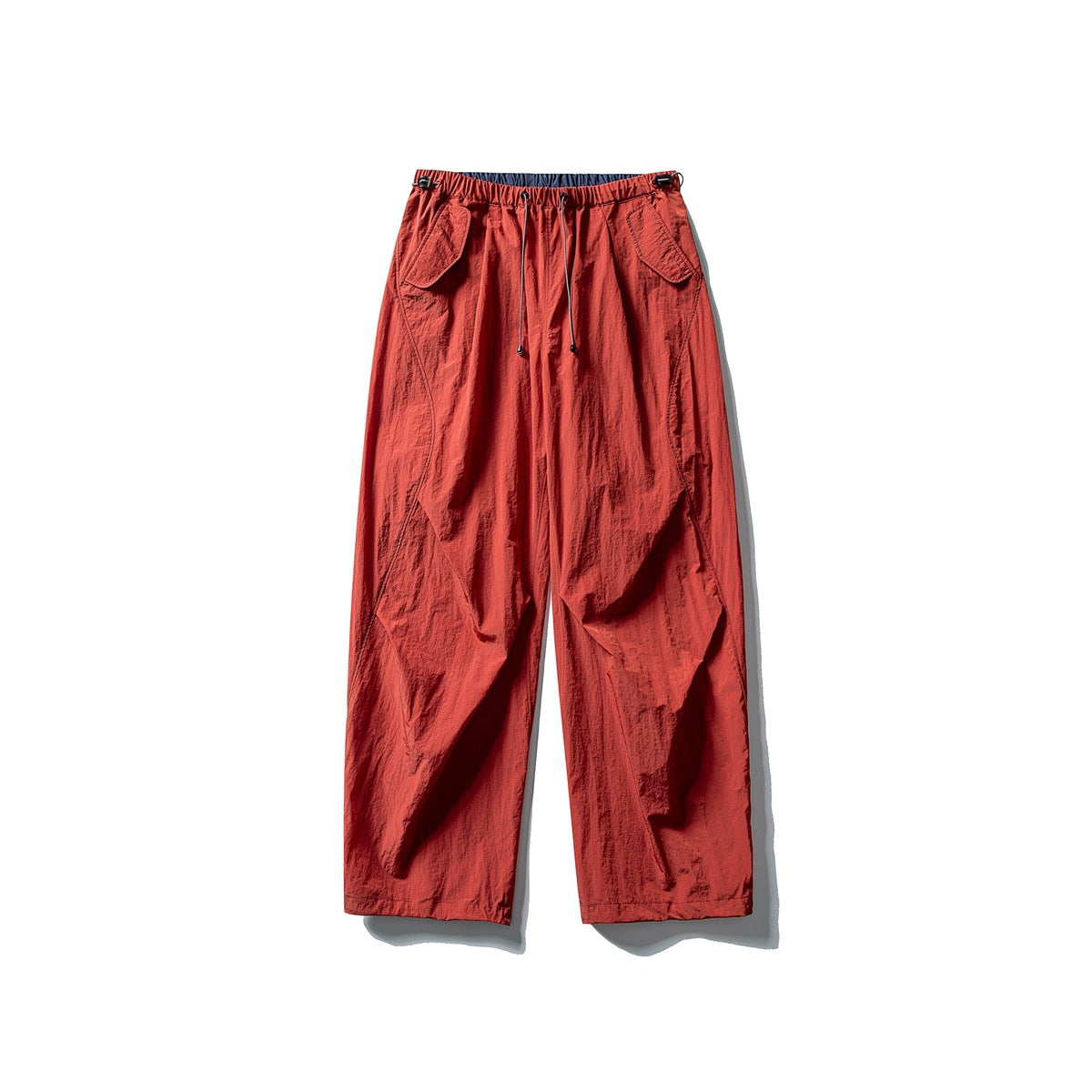 Full view of rust-red, wide-leg utility pants with an elastic drawstring waist and large flap pockets.