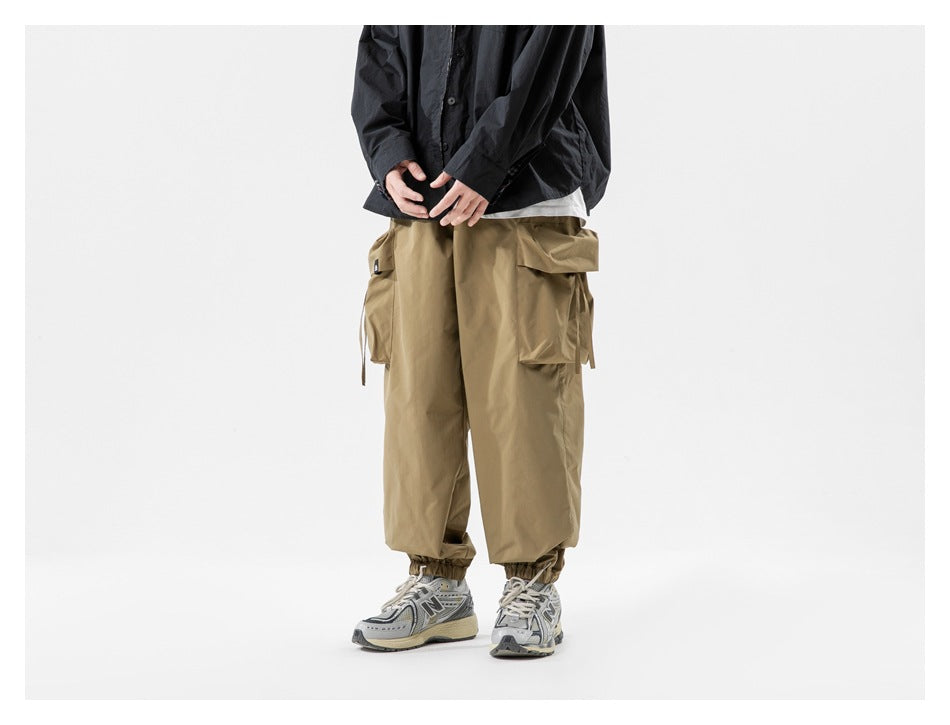 Cropped model wearing loose tan cargo pants with oversized side pockets and gathered ankle cuffs.