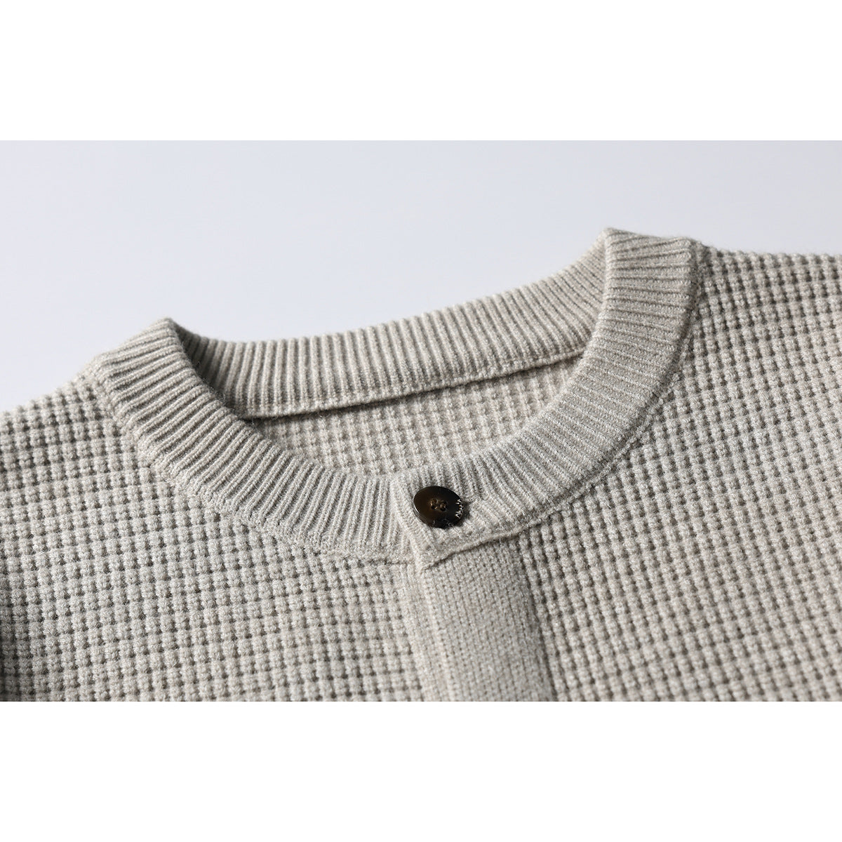 Close-up of a light gray textured knit cardigan collar and placket with a dark button.